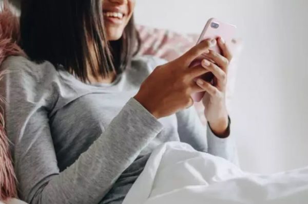 Woman holding a phone in bed while having phone sex